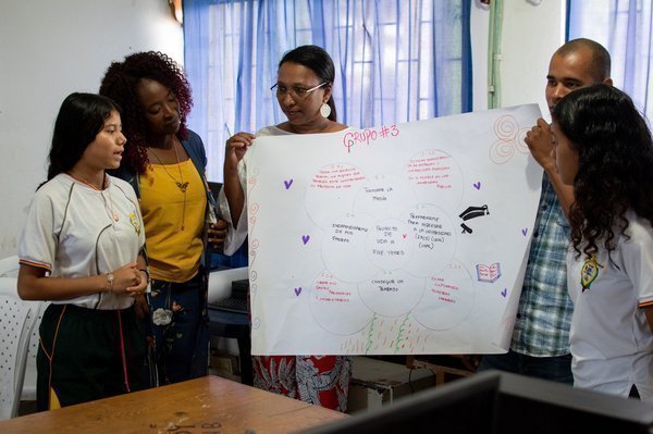 Estudiantes exponiendo con cartelera en clase