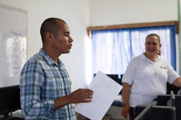 Hombre sosteniendo hoja, al fondo se ve mujer sonriendo