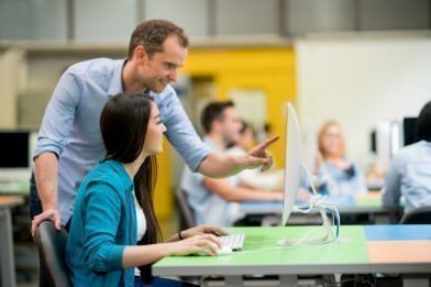 Docente con estudiante frente a un computador